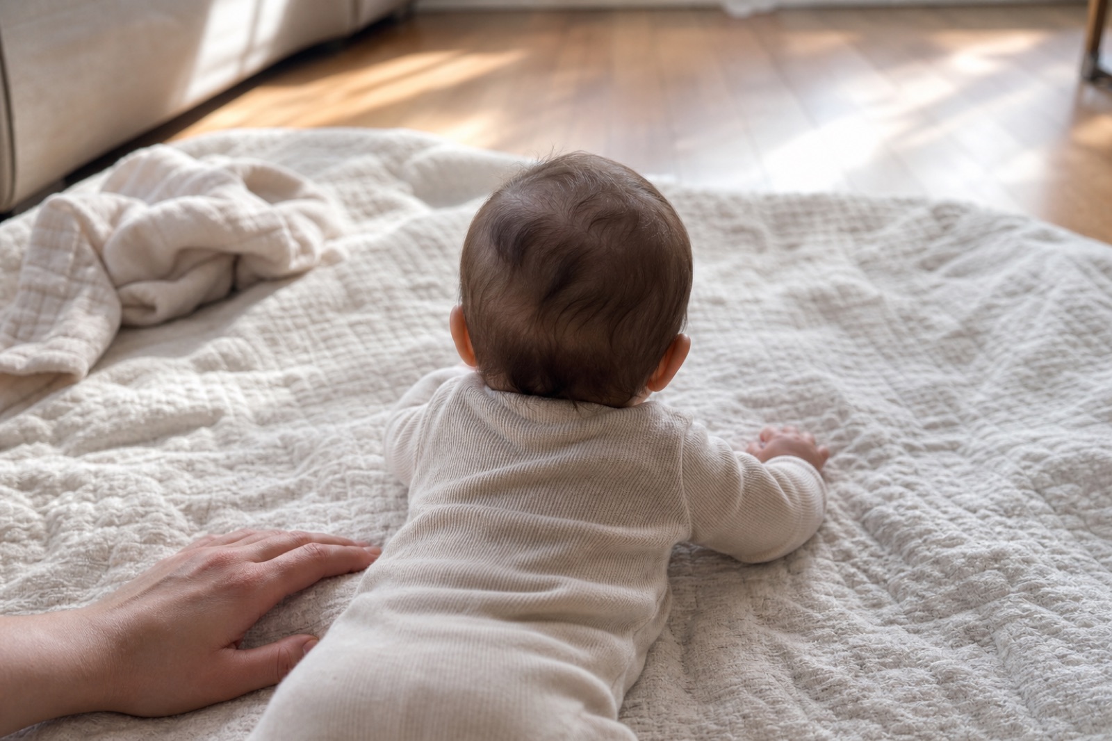 Baby seen from behind during tummy time with an adult hand nearby