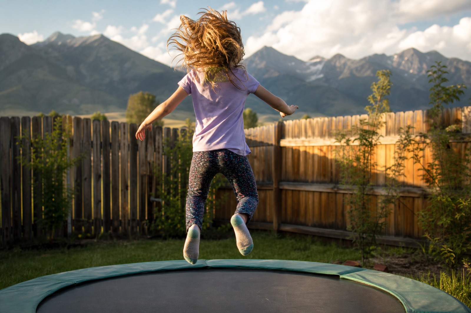 Child seen from behind jumping on a trampoline outdoors
