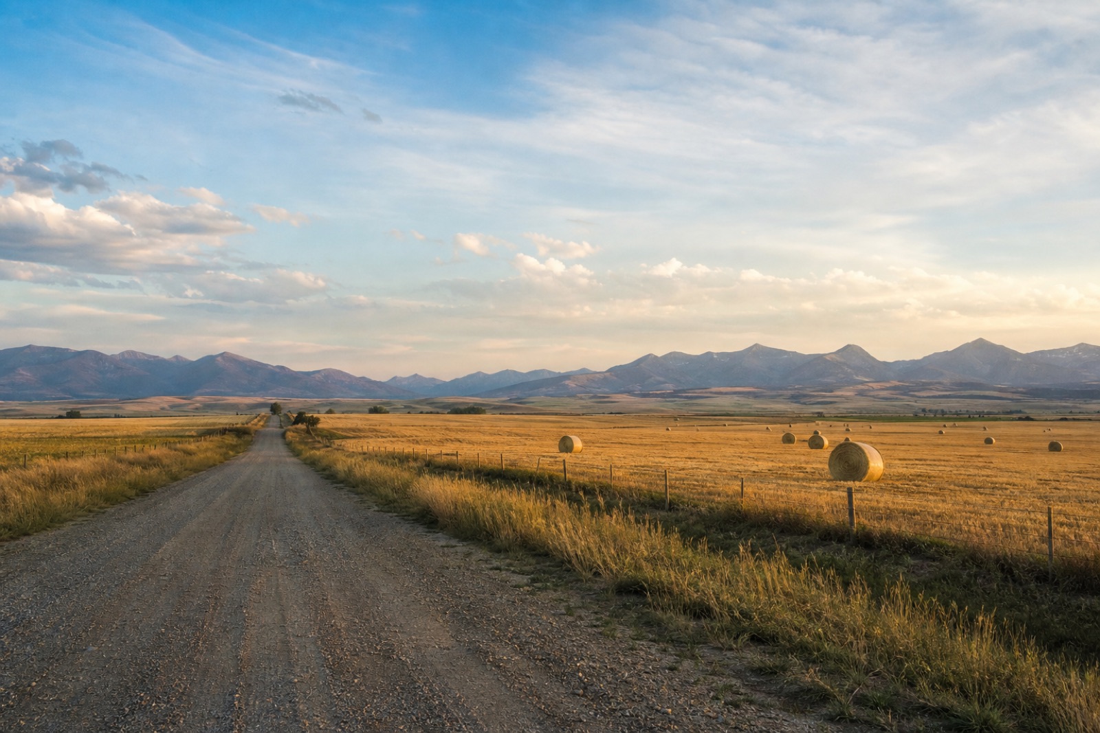 Gravel road passing fields and hay bales near Belgrade with distant mountains
