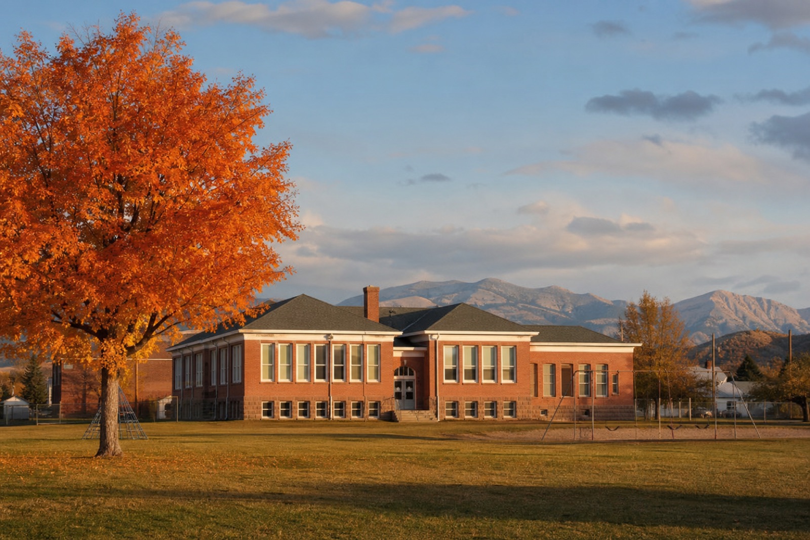 School building beneath autumn trees and mountains