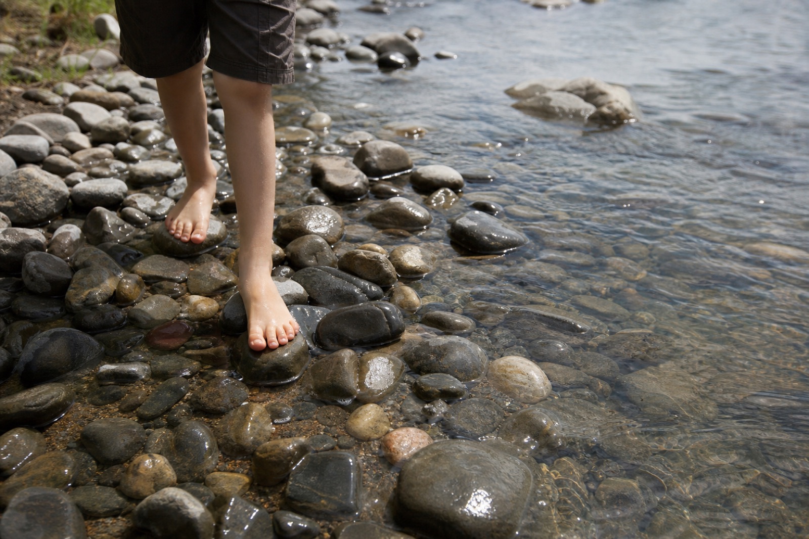 Child’s bare feet on smooth stones beside a shallow stream
